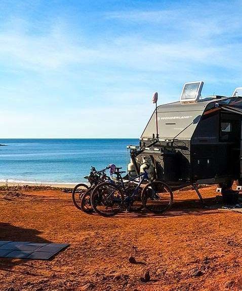 A camper trailer is parked next to a beach with bikes parked in front of it.