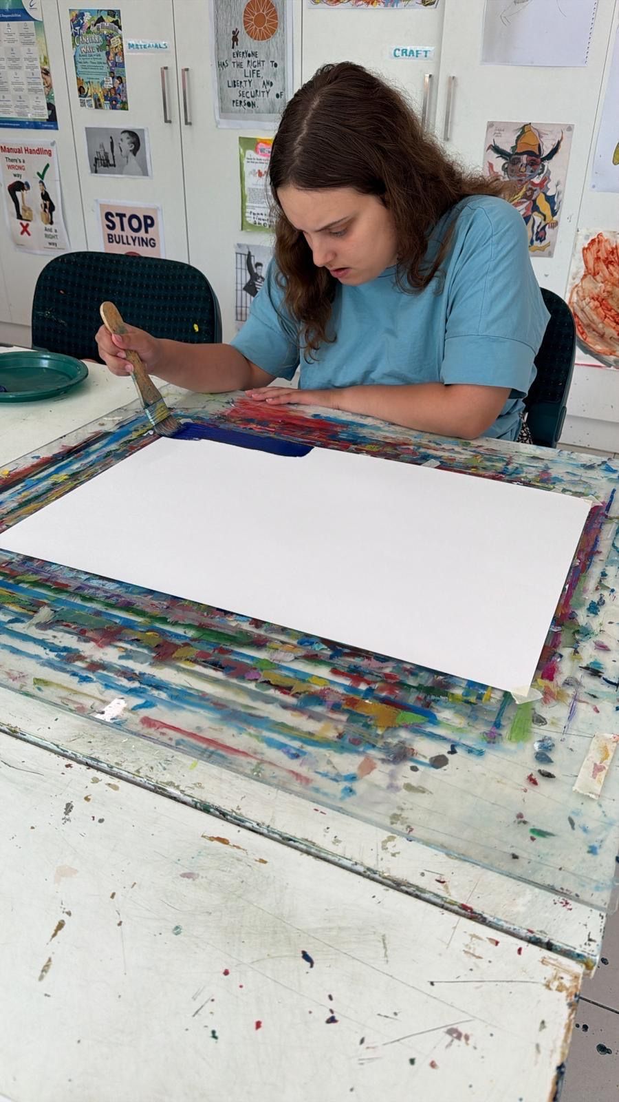 A group of children are sitting on the floor painting a sign.