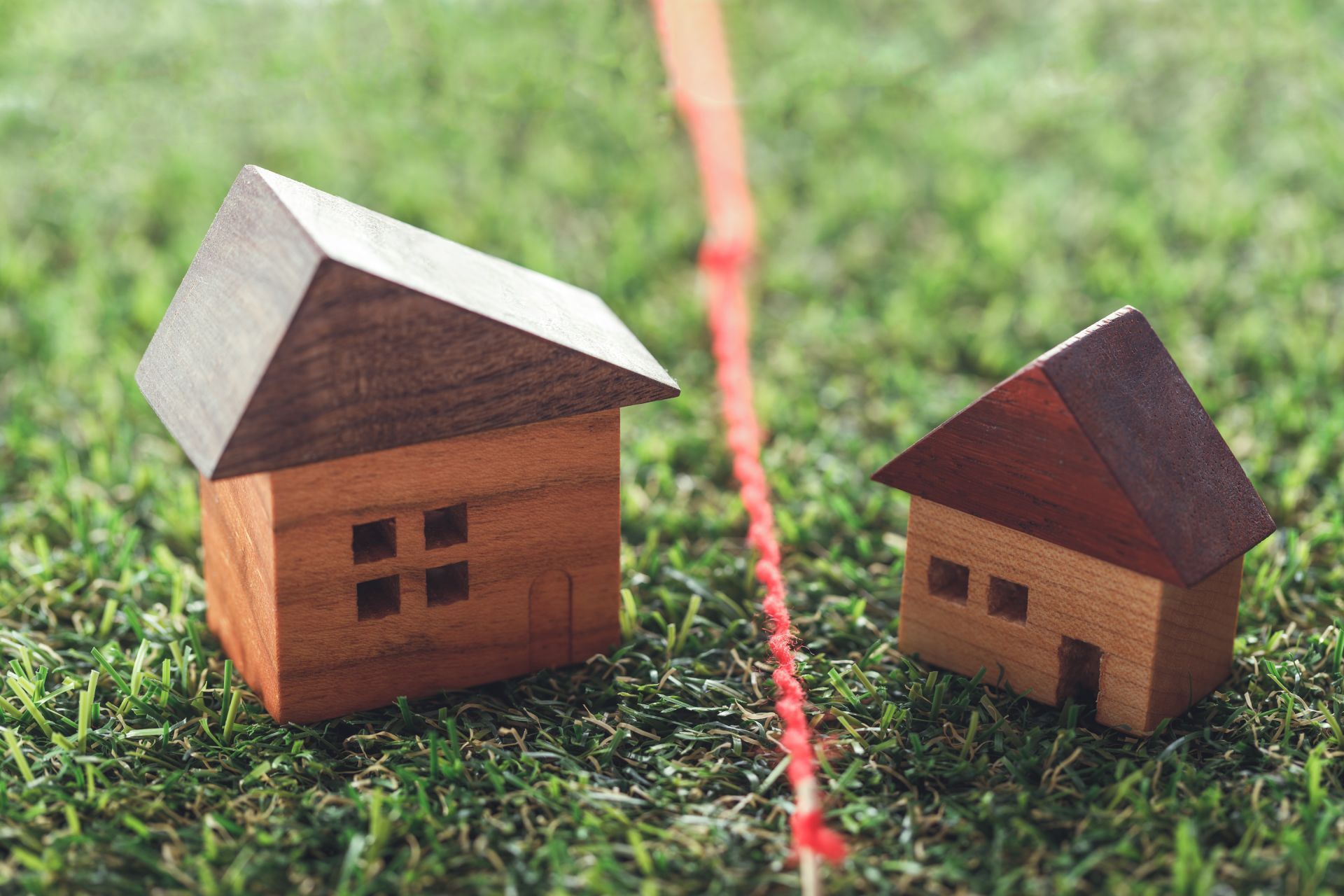 Two small wooden house models on grass, separated by a red string.