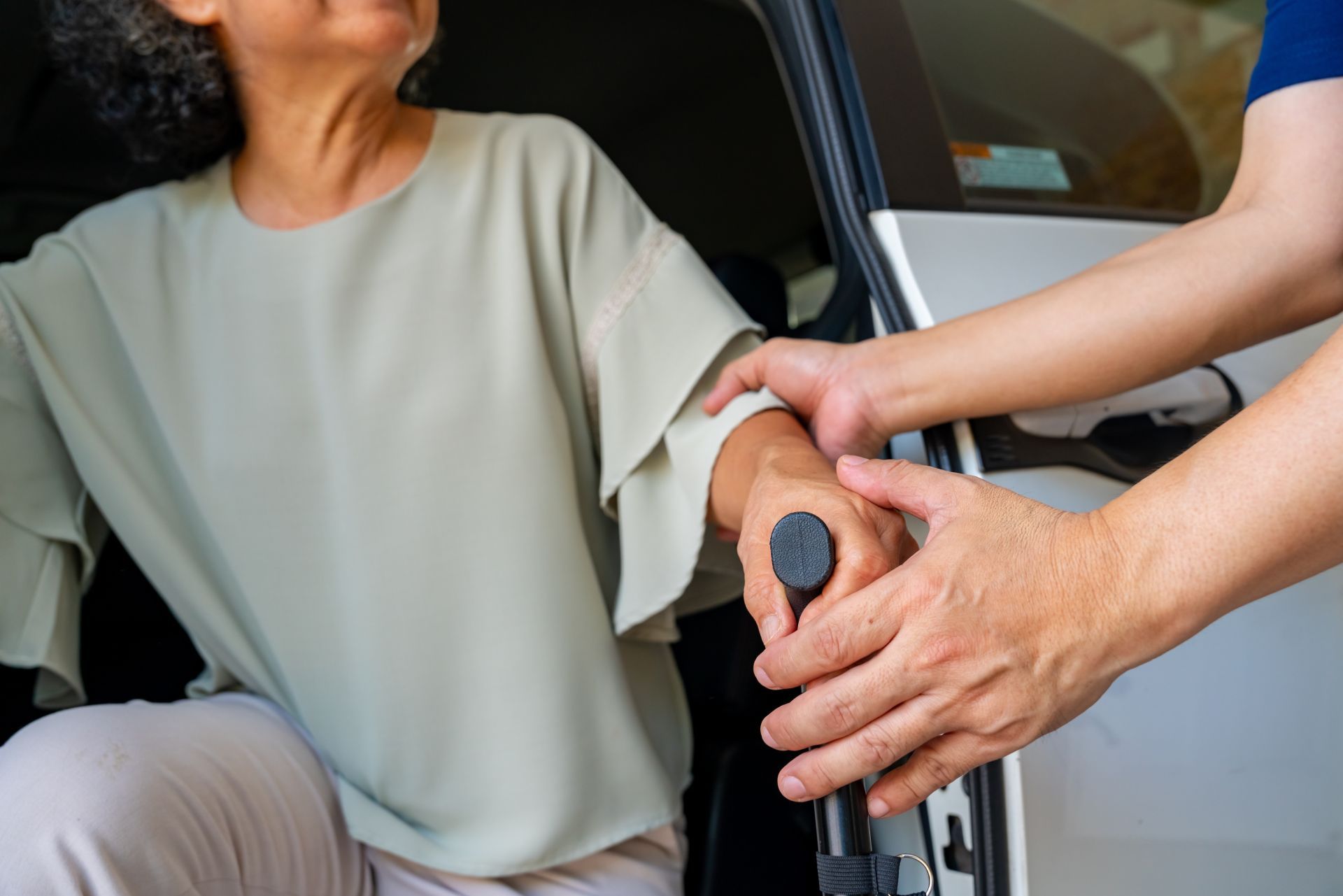 Person with cane assisted into a car by another person's hand.