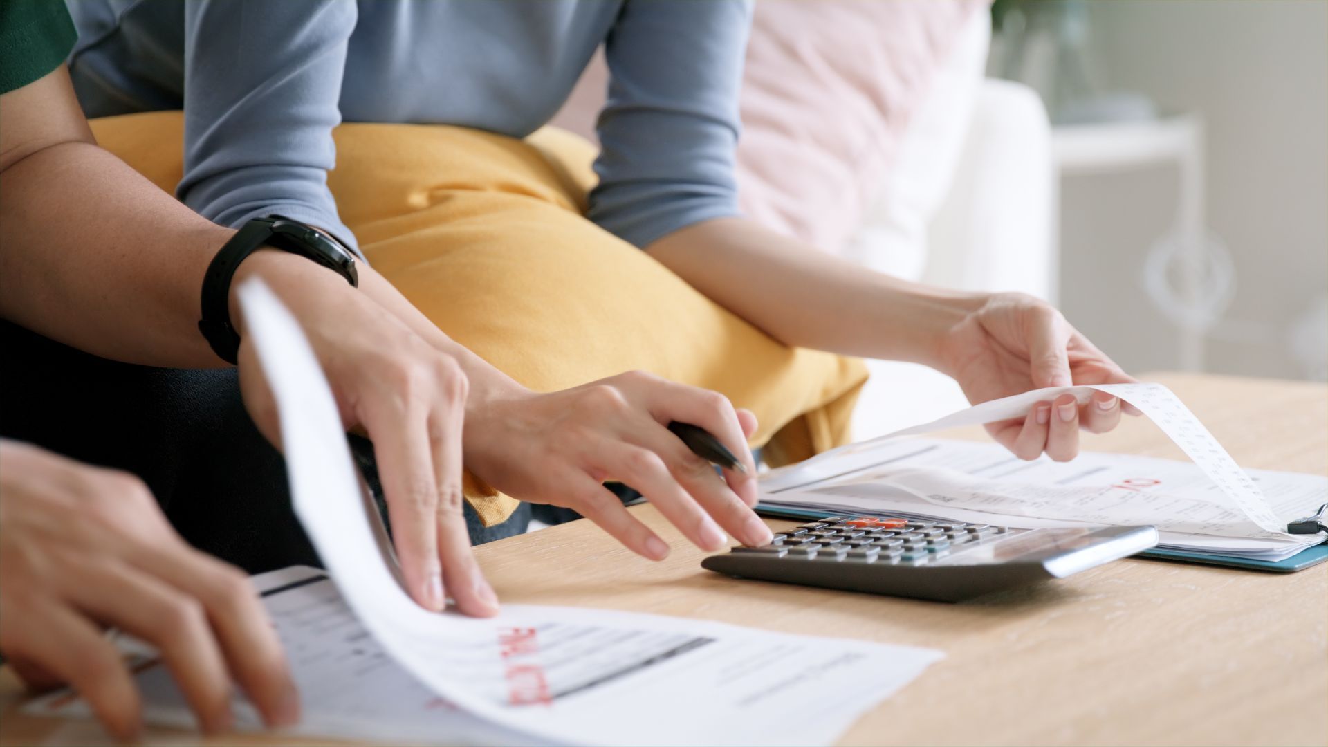 Hands using calculator and reviewing papers, possibly budgeting at a table.