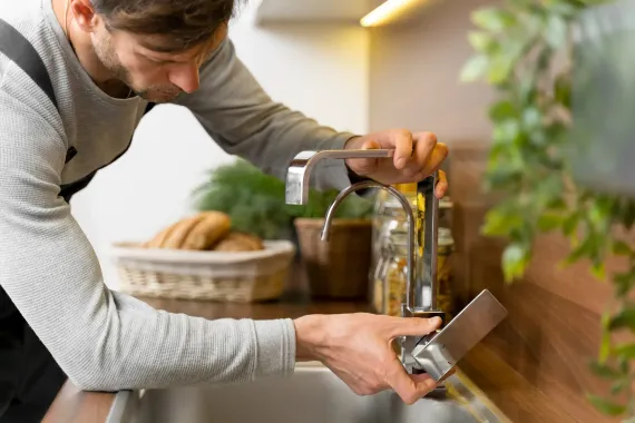 A man is fixing a faucet in a kitchen.