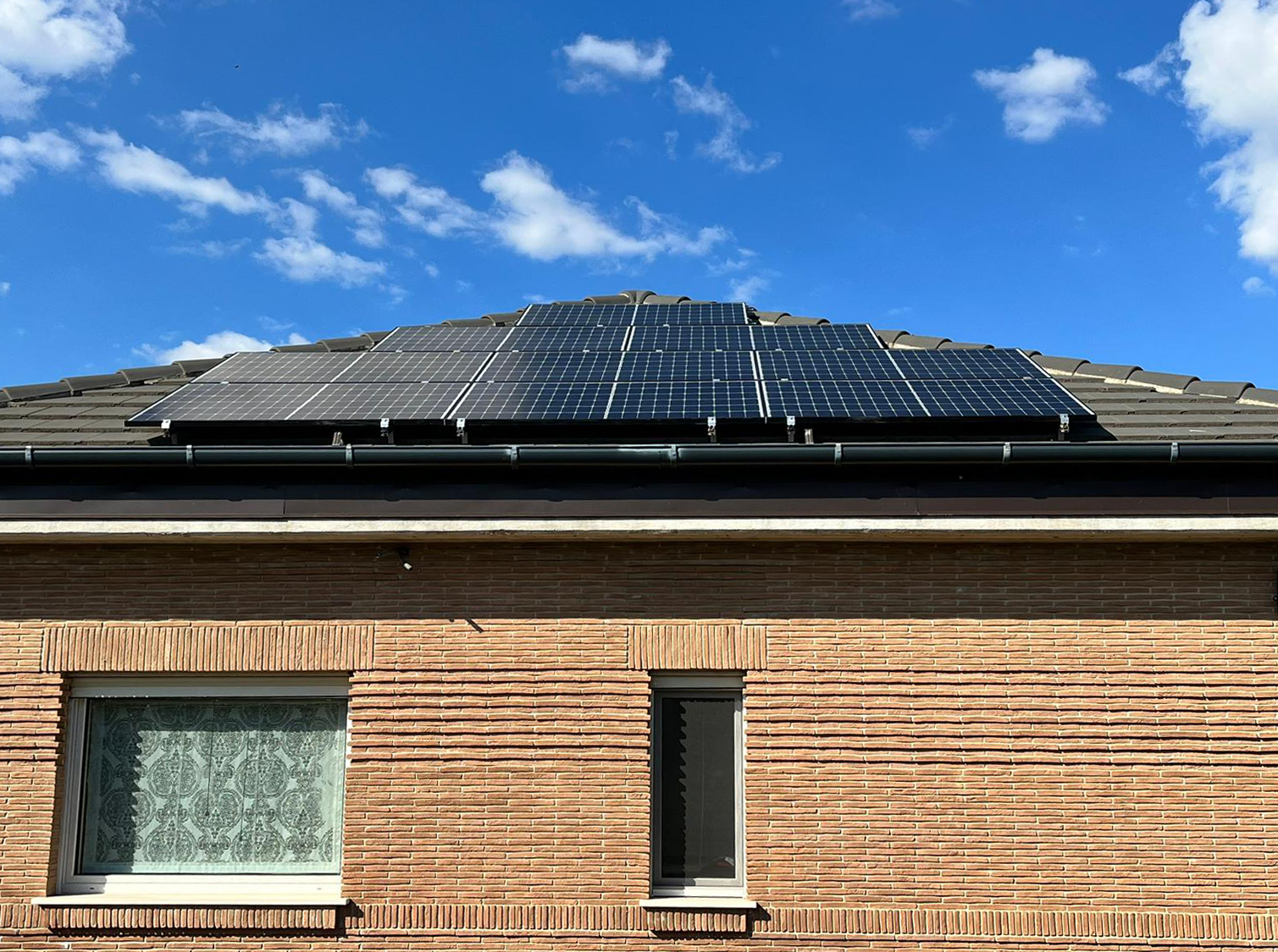 Pannelli solari sul tetto di una casa di mattoni sotto un cielo azzurro con nuvole