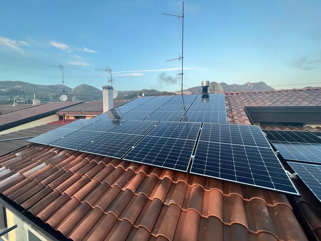 Pannelli solari sul tetto di una casa con tegole, sotto un cielo azzurro e limpido.