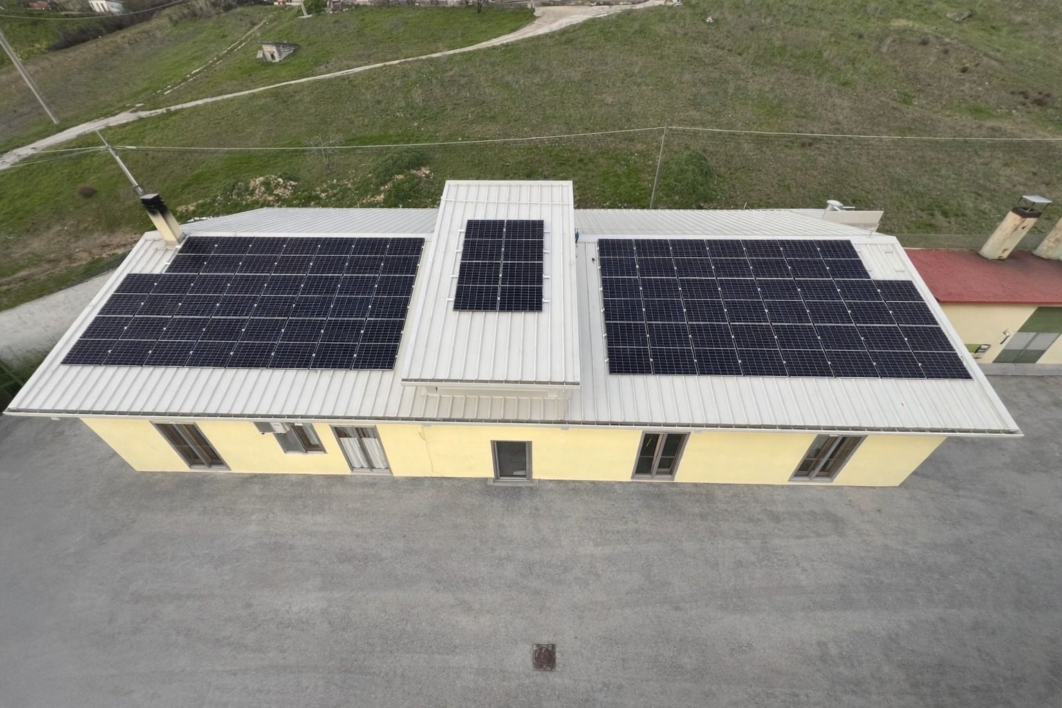 Veduta aerea del tetto di un edificio con pannelli solari e una piccola struttura centrale sul tetto.