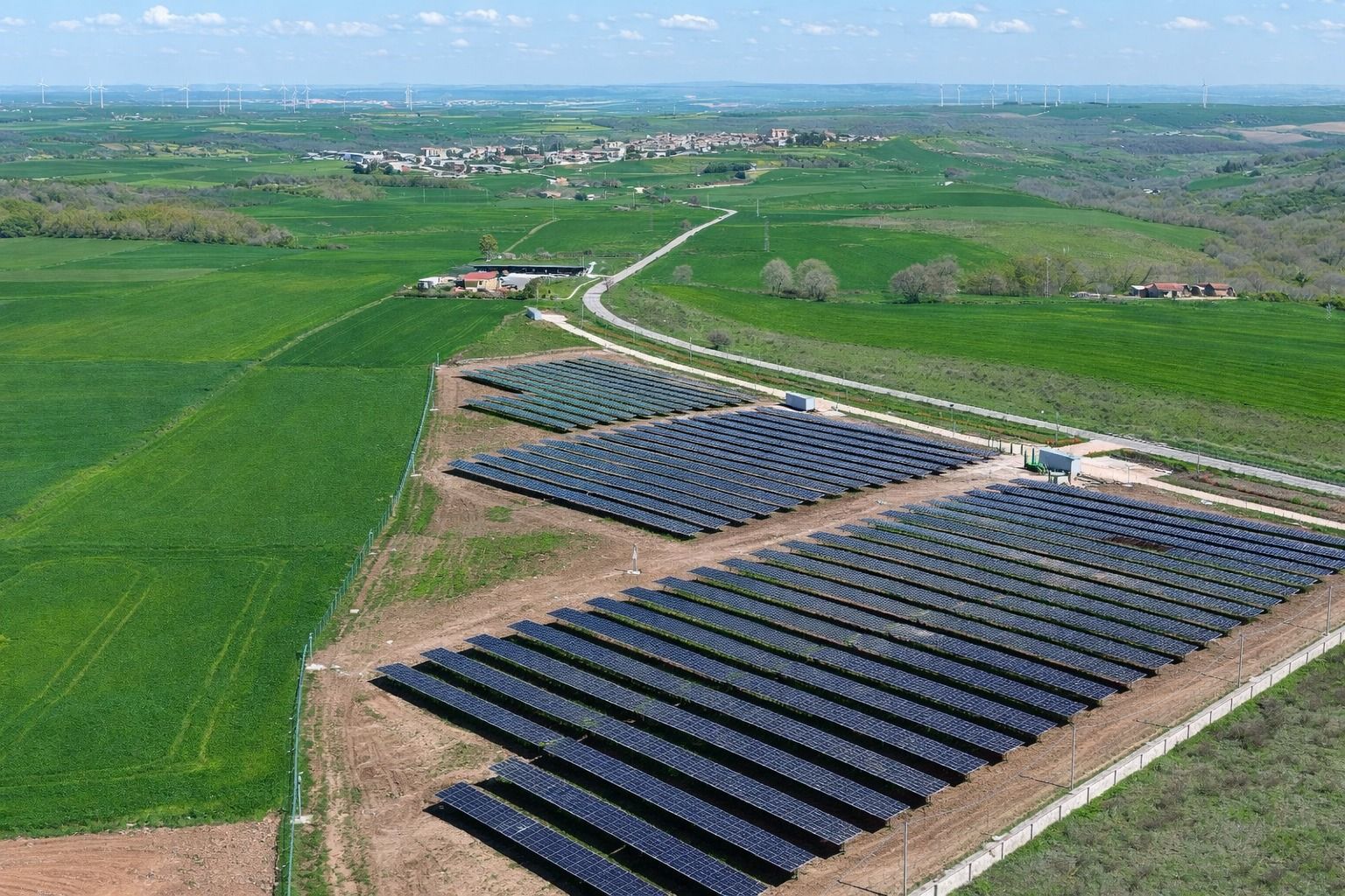 Pannelli solari disposti in file in un verde paesaggio rurale sotto un cielo azzurro