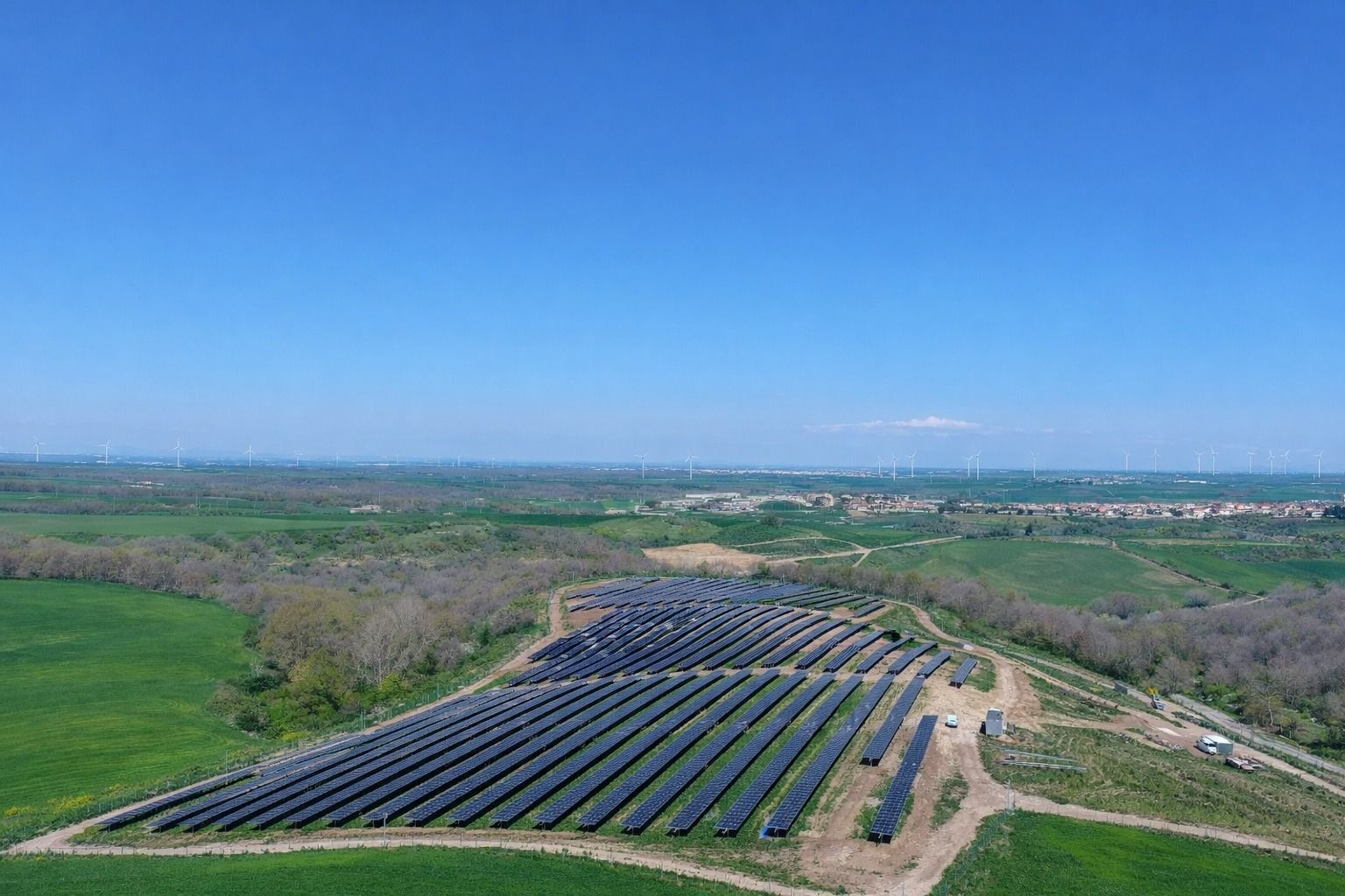 Veduta aerea di un impianto solare con file di pannelli blu in un verde paesaggio rurale sotto un cielo limpido.
