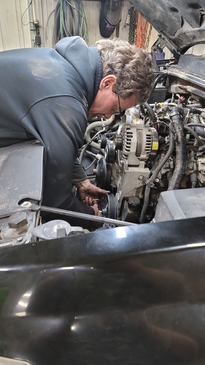 Mechanic in a dark hoodie working under the hood of a car in a garage 