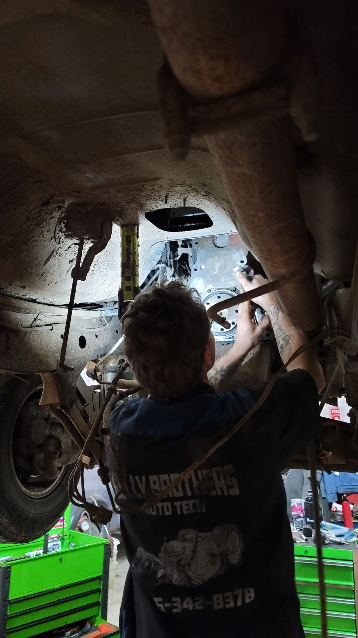 Person working inside a vehicle chassis during repairs, with tools and a lit garage background | Belly Brothers Auto Tech