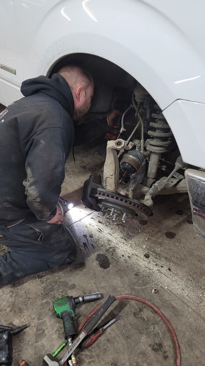 Mechanic repairing a car wheel well with tools on the ground beside a white vehicle | Belly Brothers Auto Tech
