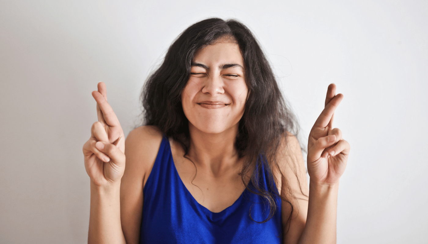 A woman in a blue tank top is crossing her fingers.