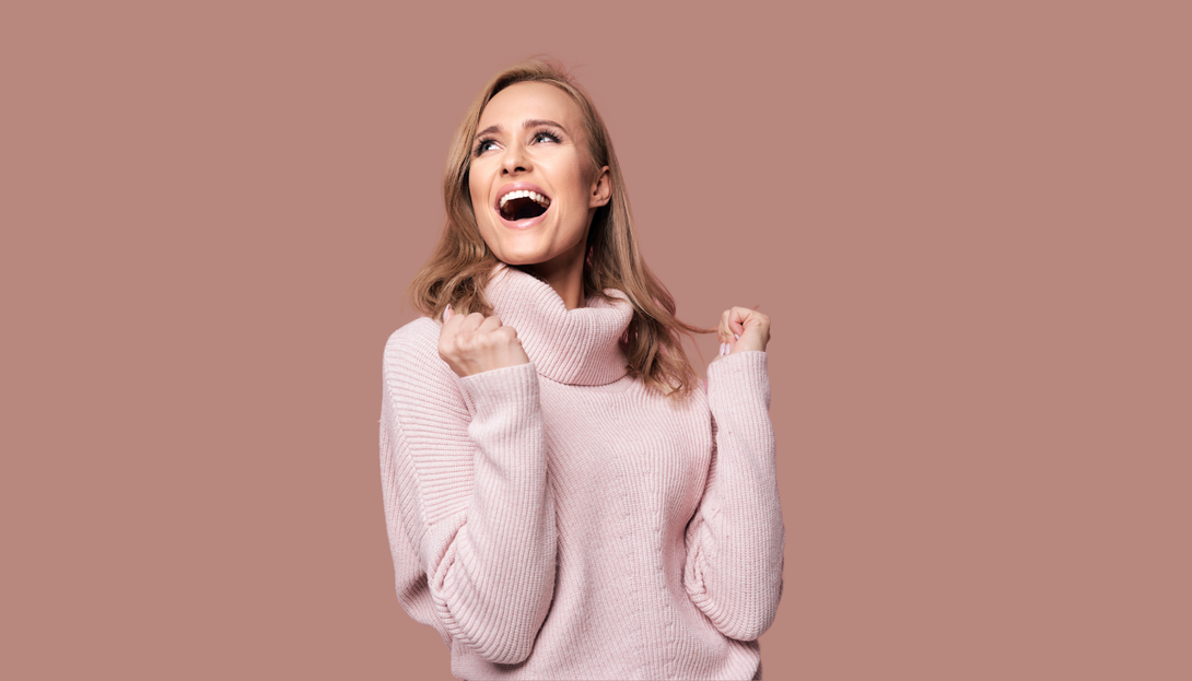 A woman in a pink sweater is laughing and looking up.