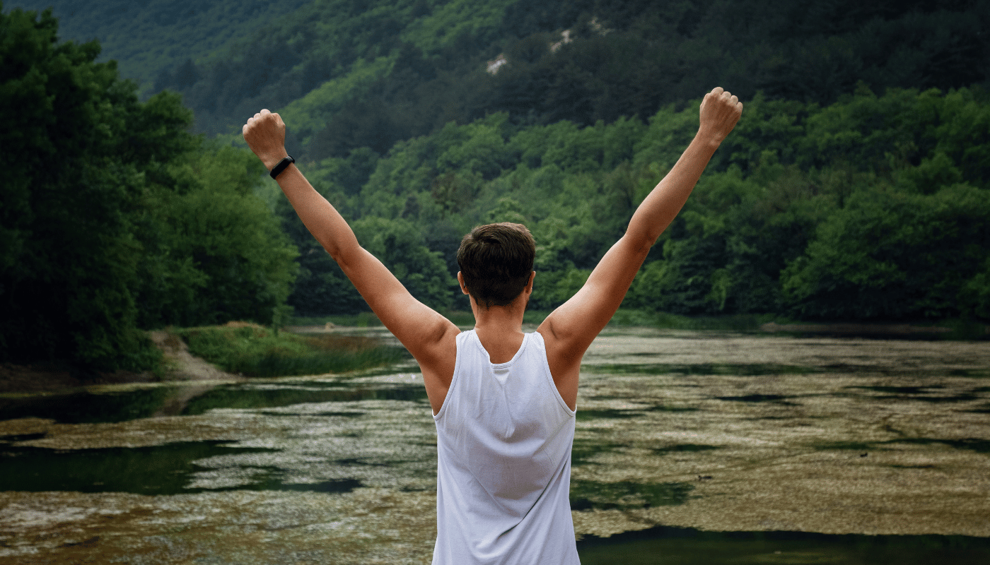 A man is standing in front of a river with his arms in the air.