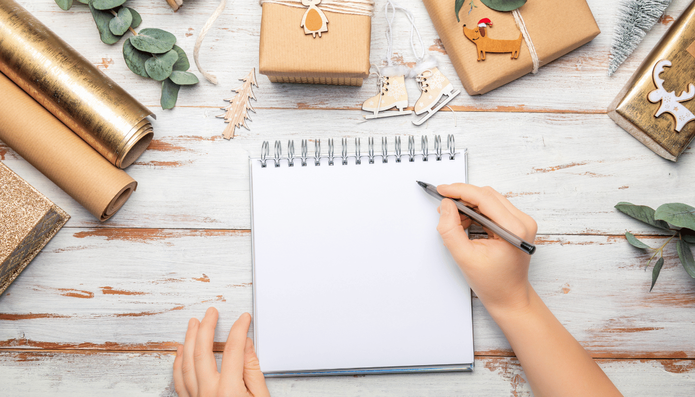 A person is writing in a notebook on a wooden table.