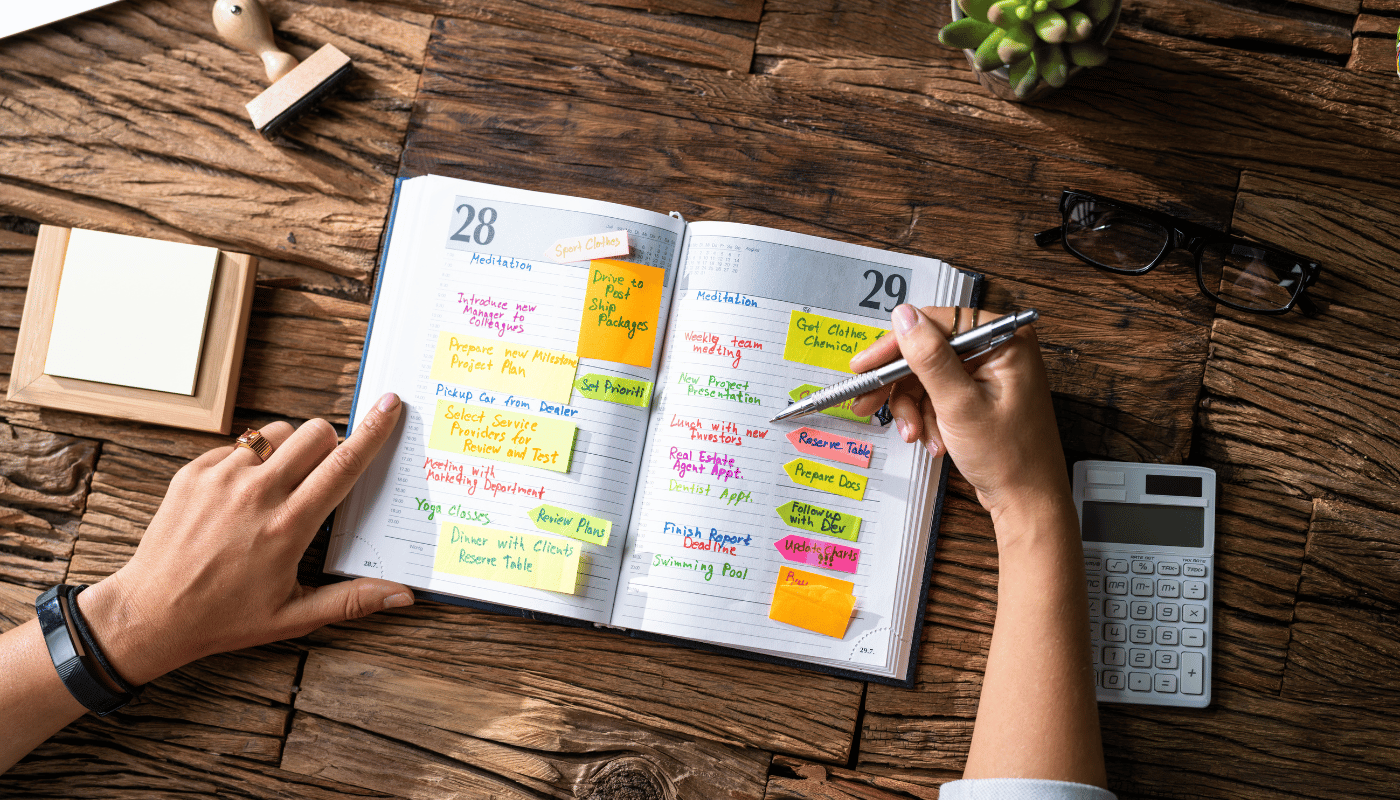 A person is writing in a notebook with sticky notes and a pen.