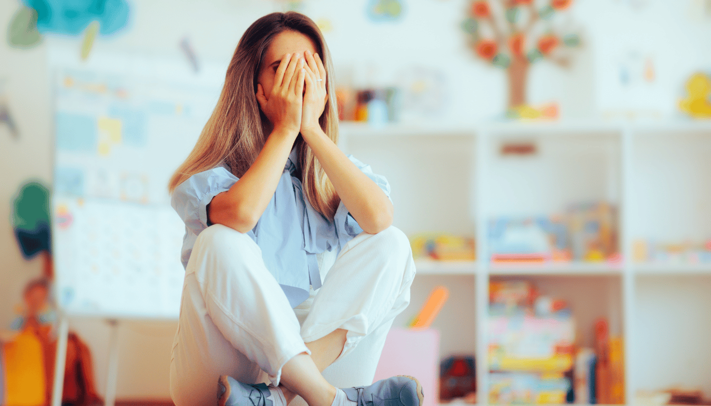 A woman is sitting on the floor covering her face with her hands.