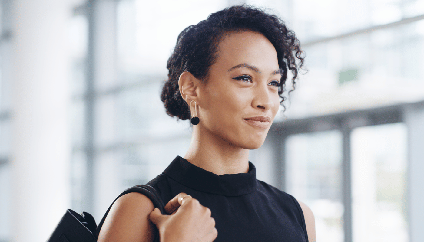 A woman in a black dress is holding a purse and smiling.
