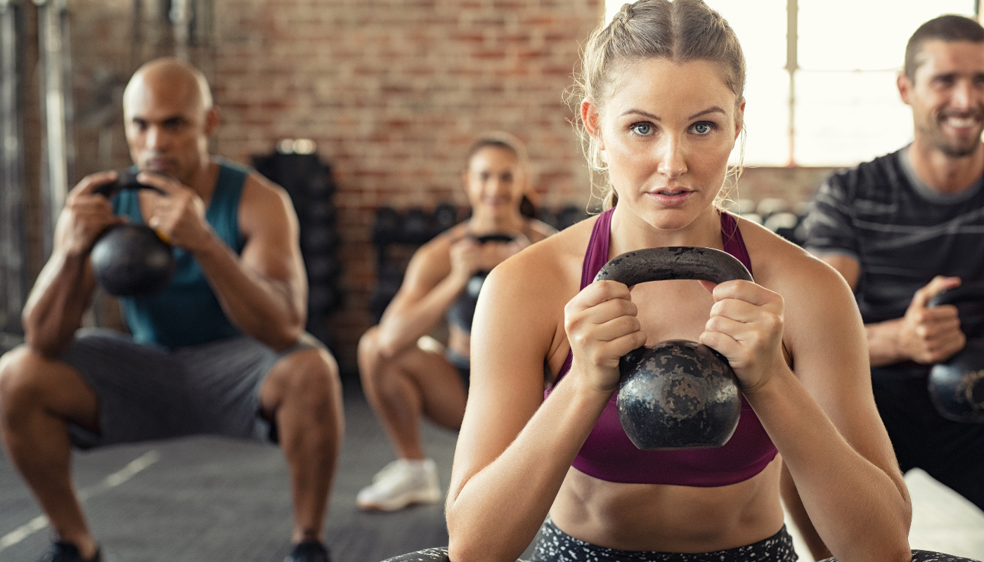 A group of people are squatting with kettlebells in a gym.
