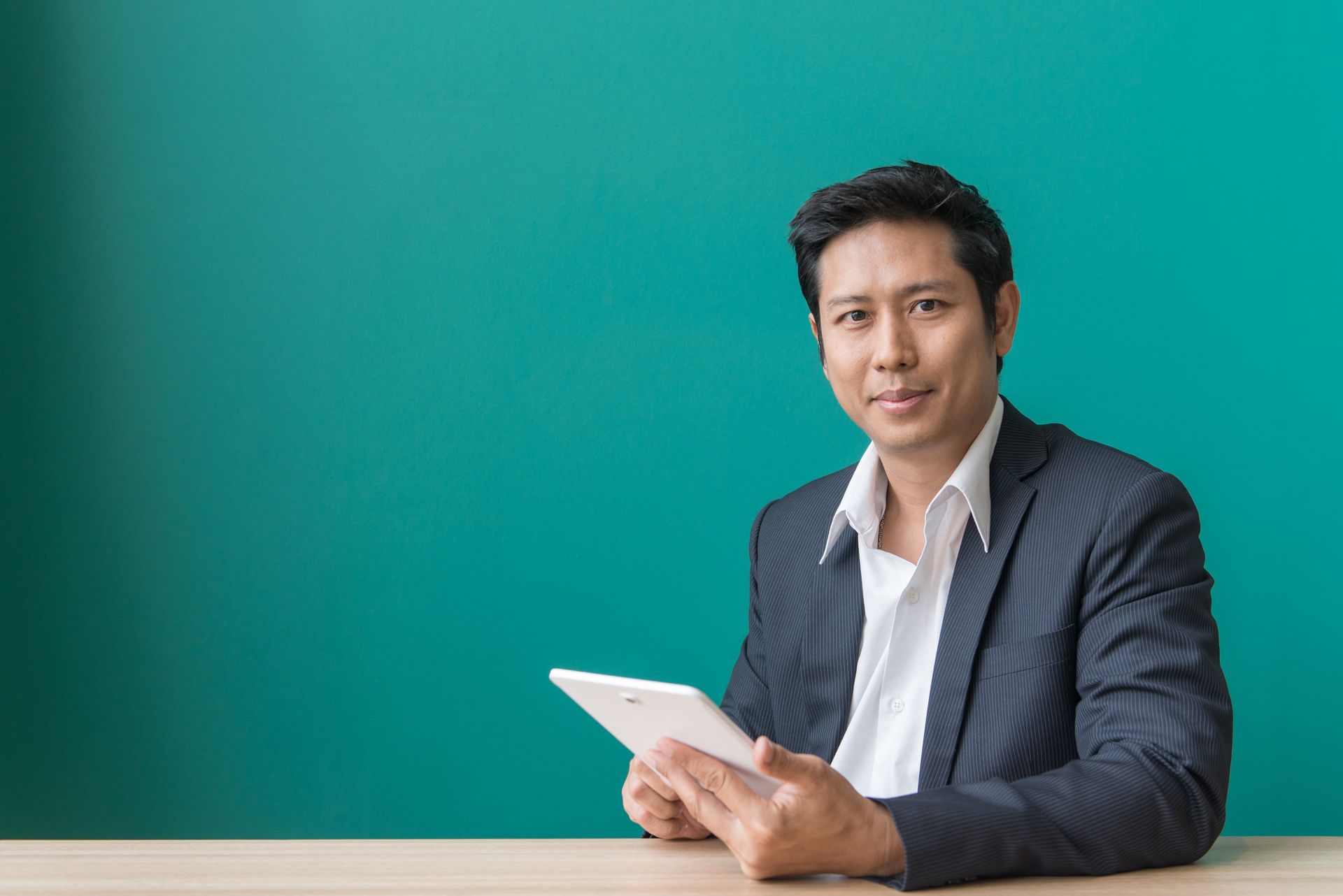 A man in a suit is sitting at a table holding a tablet computer.
