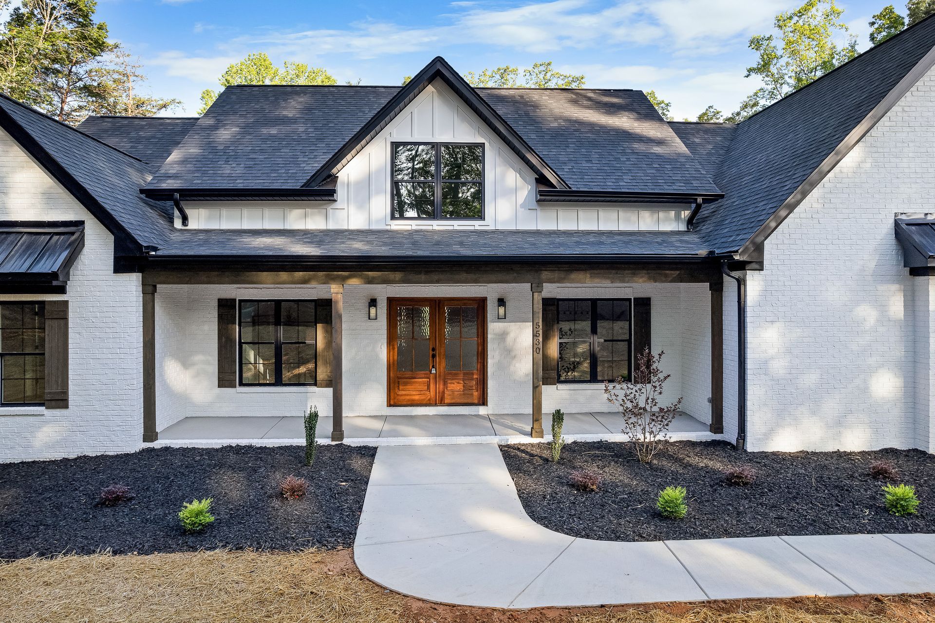 A white house with a black roof and a walkway leading to it.