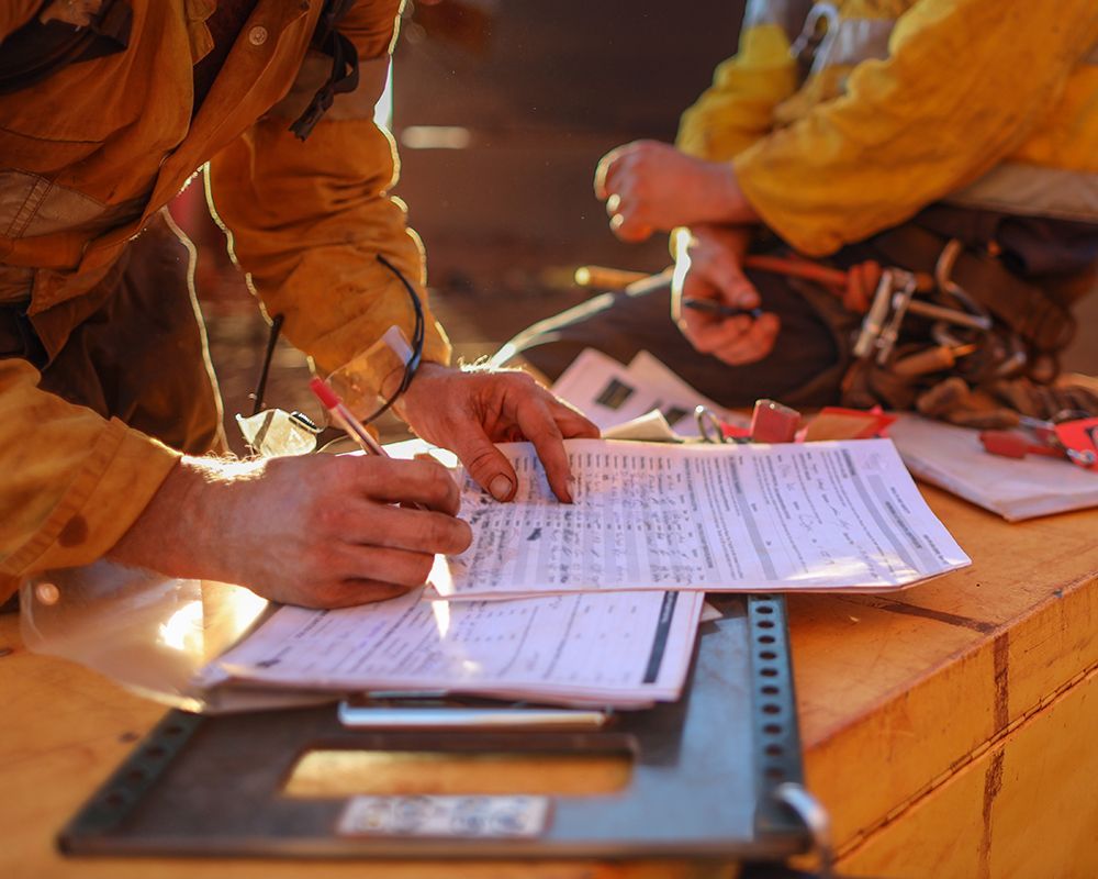 A man in a yellow jacket is writing on a piece of paper