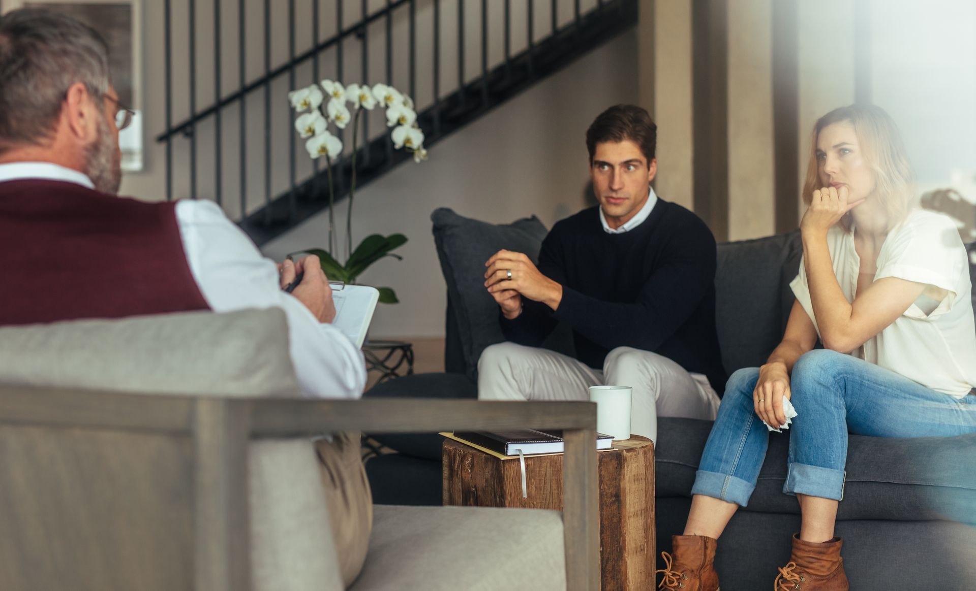 Couple in counseling session; therapist taking notes. Modern interior, concerned expressions. Couple in counseling session; therapist taking notes. Modern interior, concerned expressions.
