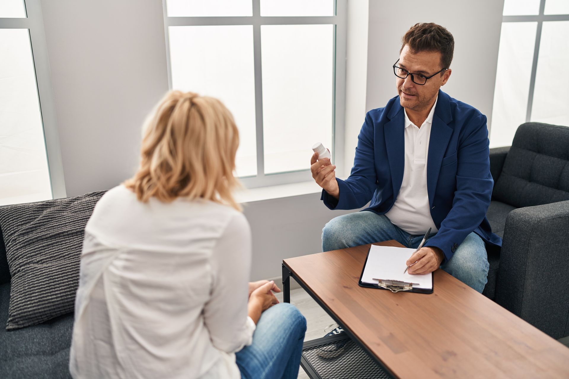 A therapist showing medication to a client in a counseling session. The office has a couch and window.
