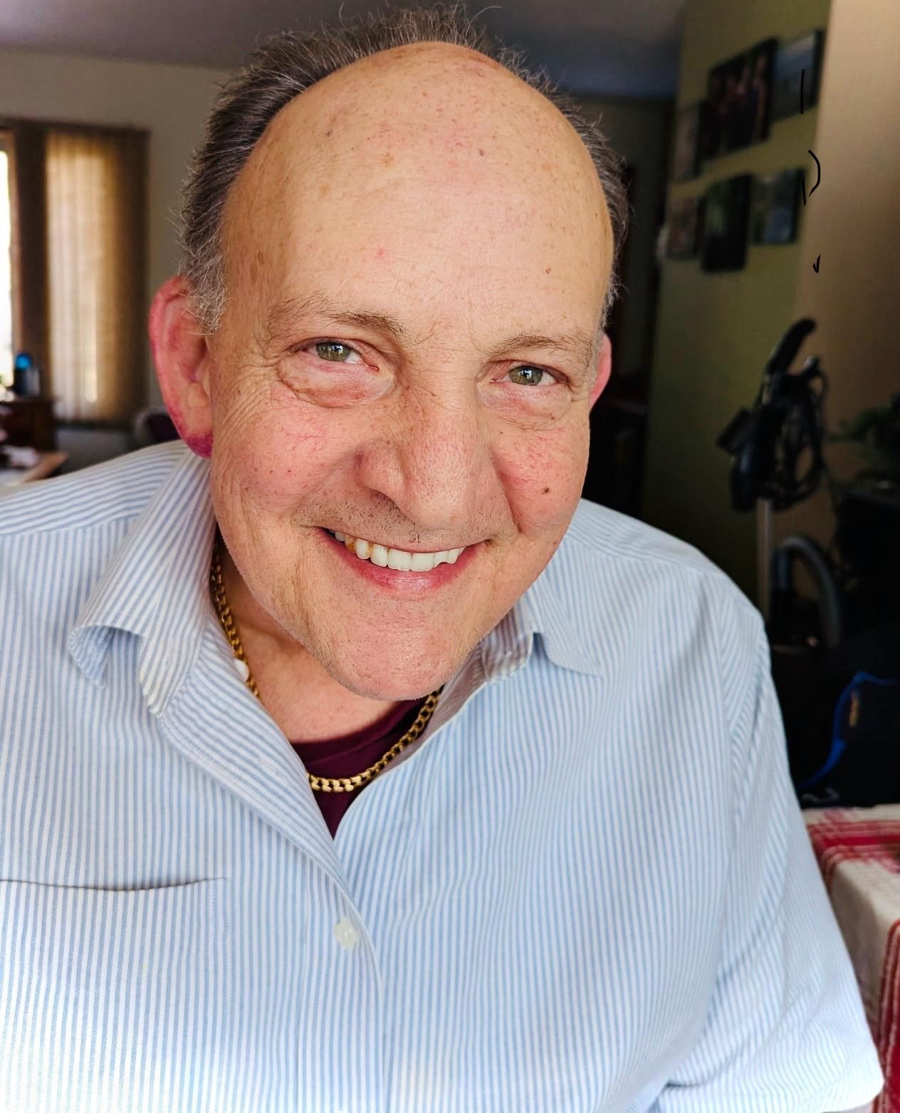 Man smiling, wearing a light blue striped button-down shirt. Gold chain visible. Man smiling, wearing a light blue striped button-down shirt. Gold chain visible.