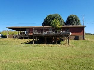 A red house with a large deck is sitting on top of a lush green field.