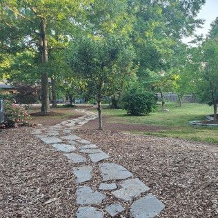 Stone path winding through a leafy park with trees, mulch, and green grass