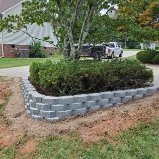 Mulched yard bed with shrubs edged by gray retaining blocks beside a suburban driveway