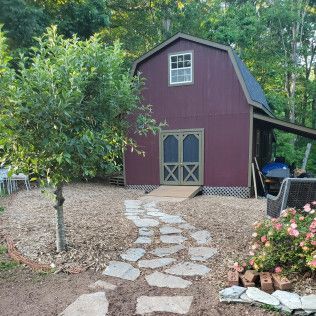 Maroon shed with double doors and stone path in a wooded backyard garden