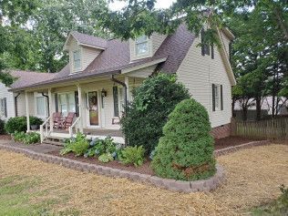 A white house with a porch and a fence in front of it.