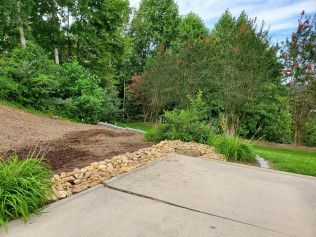 A concrete driveway leading to a grassy hillside with trees in the background.