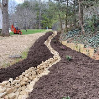 Mulched garden bed bordered by rocks beside a lawn, with a small orange loader in the background