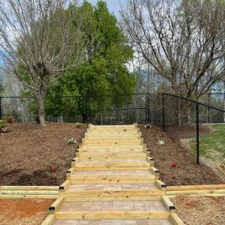 Wooden steps leading up a landscaped path between fenced yards with trees and mulch