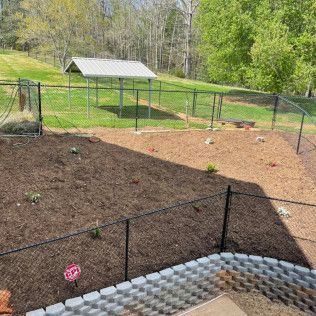 Backyard with black fence, mulched garden beds, grassy yard, and a small shed in the distance