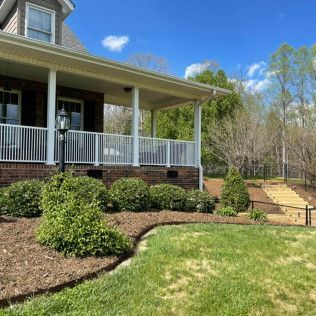 Front porch with white railing, landscaped shrubs, and a grassy yard beside a stone path and steps