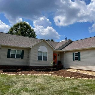 Single-story beige house with a gray roof, front lawn, and cloudy blue sky.