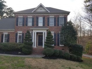 A large brick house with black shutters and trees in front of it.