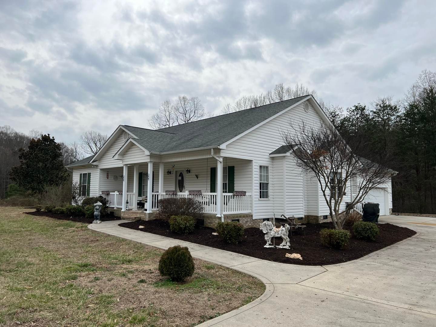 White house with a front porch, curved driveway, and landscaped yard under a cloudy sky