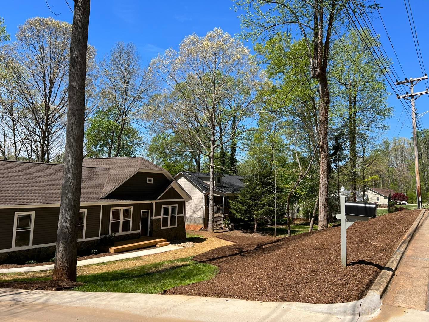 Brown house beside railroad tracks under a clear blue sky, with trees and utility poles nearby.