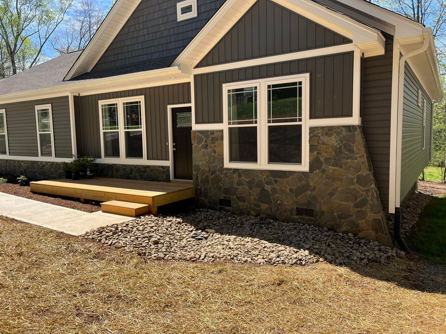 Gray house with stone and siding exterior, white-trim windows, and a small front porch over a gravel bed.