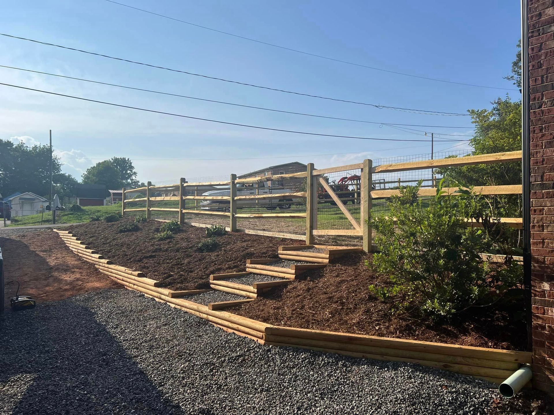 Wooden fence and steps along a landscaped gravel path on a sunny hillside