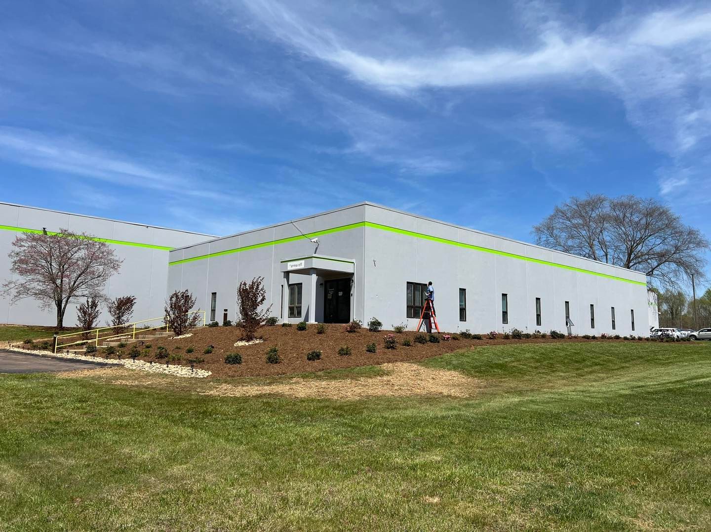 White industrial building with green trim on a grassy lot under a blue sky