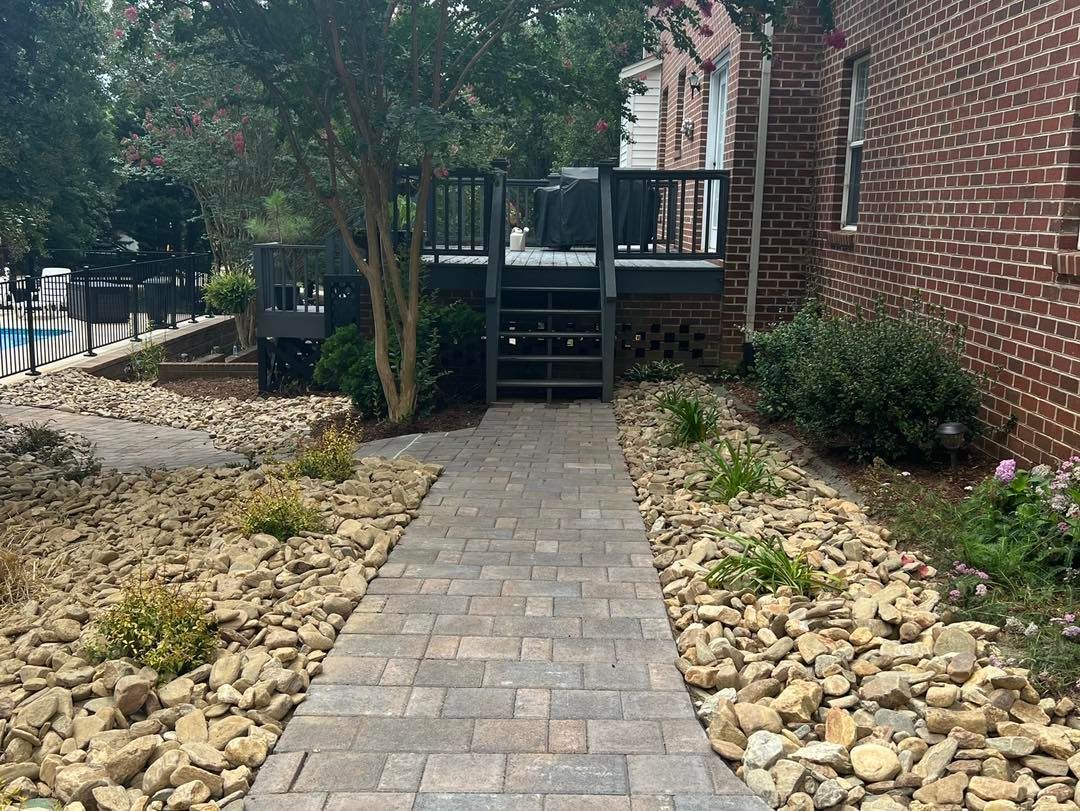 Brick walkway between landscaped rock beds leading to a wooden deck beside a brick building