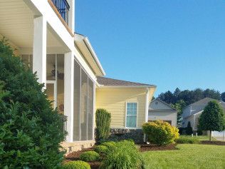 A house with a screened in porch and a large lawn in front of it.