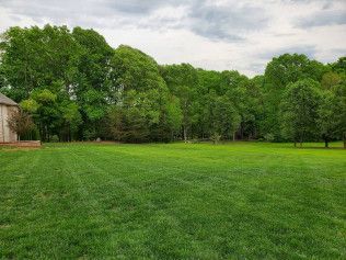 A large lush green field with trees in the background and a house in the background.