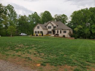 A large house is sitting on top of a lush green field surrounded by trees.