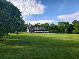 A large house is sitting in the middle of a lush green field surrounded by trees.